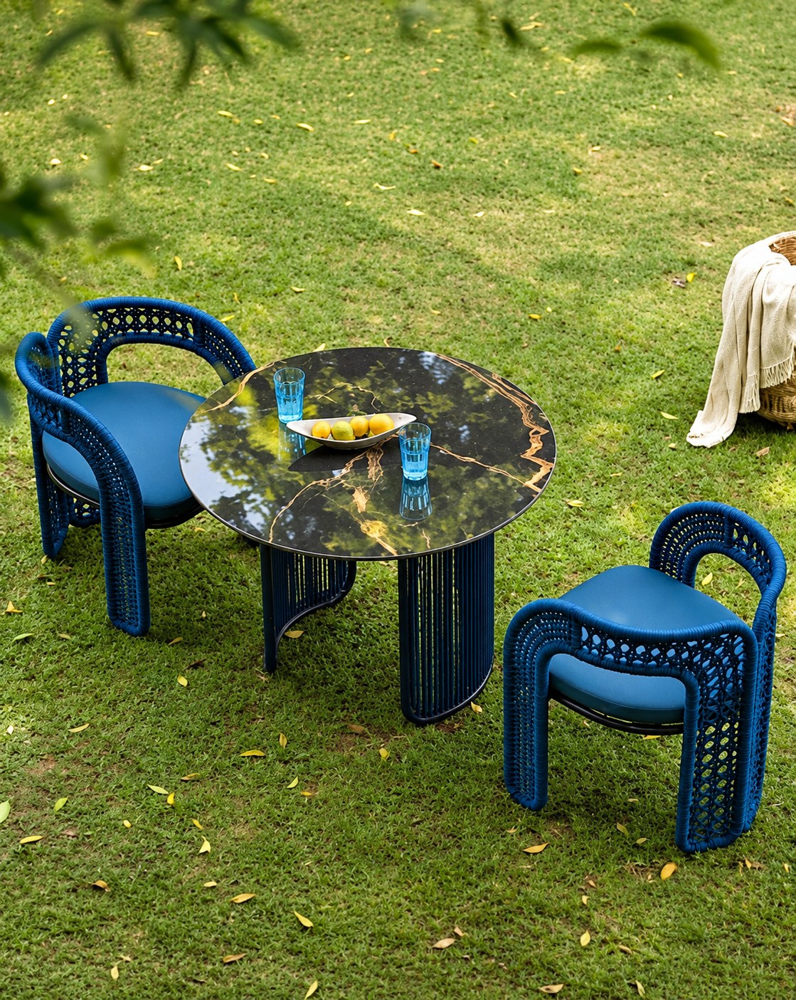 Two blue woven rope armchairs and a marble-topped table set on a lawn